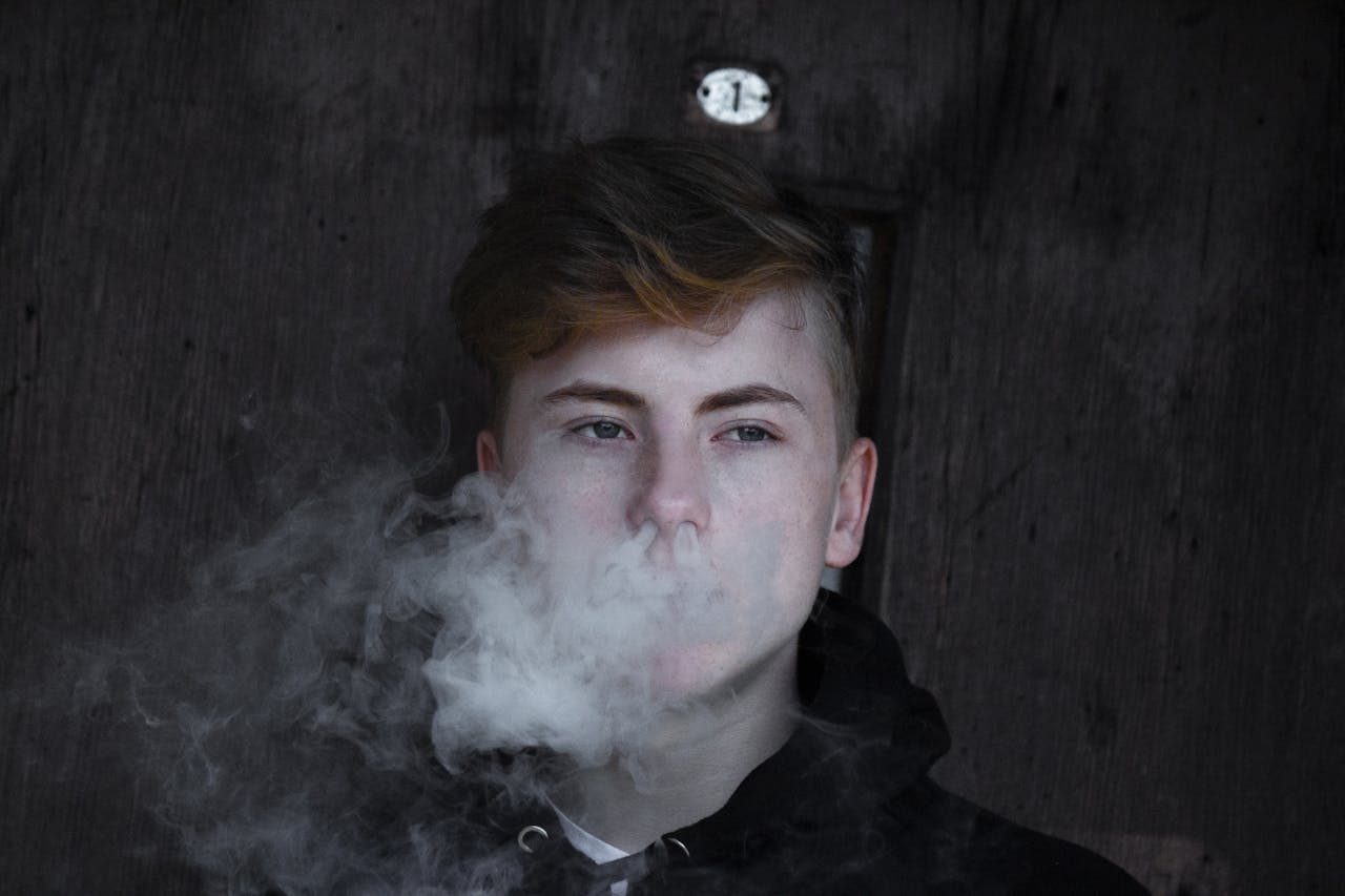 Young man exhaling a large cloud of vapor smoke against a dark wooden background