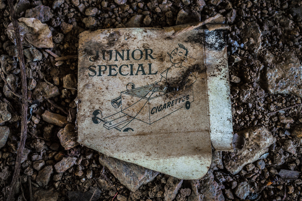 Weathered Junior Special cigarette pack lying on dirt and debris